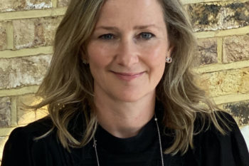 Mel Exon, WACL Campaigning Chair 2021/22, author of this article, wears a black top sitting against a brick wall.